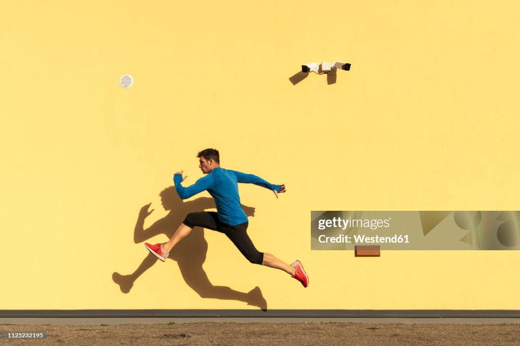 Sportive man exercising at yellow wall with CCTV camera