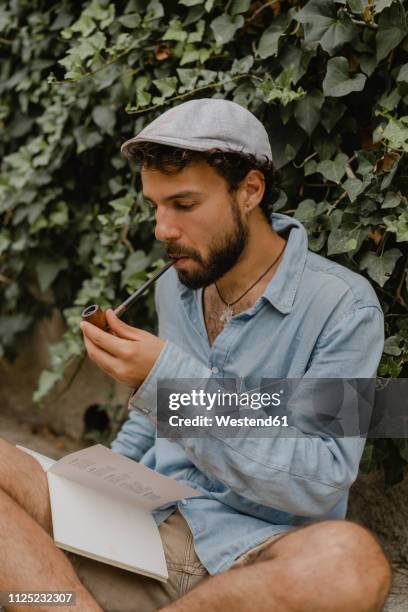 young man smoking pipe, reading a book - poeta imagens e fotografias de stock