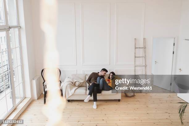 couple sitting on the couch in the living room of new home looking at cell phone - new sofa stock pictures, royalty-free photos & images