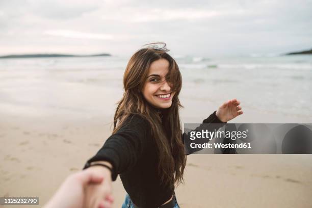 portrait of smiling young woman holding hands on the beach - brown hair blowing stock pictures, royalty-free photos & images