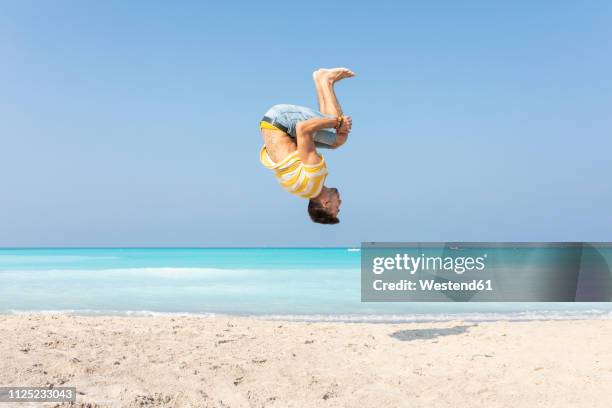 young man doing a somersault on the beach - somersault stock pictures, royalty-free photos & images