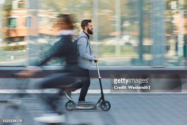 businessman riding scooter along office building - in movimento foto e immagini stock