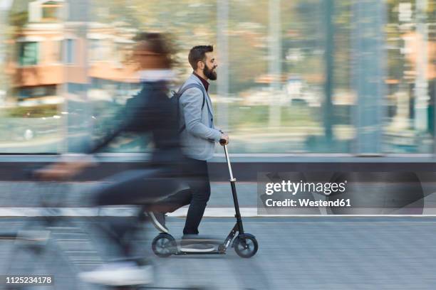 businessman riding scooter along office building - trotinete imagens e fotografias de stock