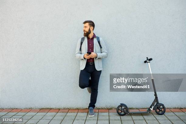 businessman with scooter and cell phone leaning against a wall - leaning stock pictures, royalty-free photos & images
