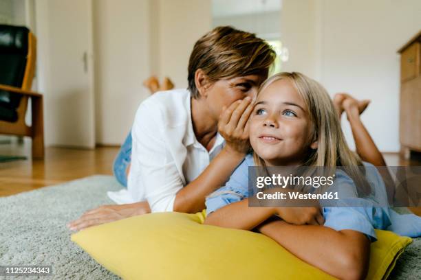 mother and daughter lying on the floor at home whispering - child whispering stock-fotos und bilder