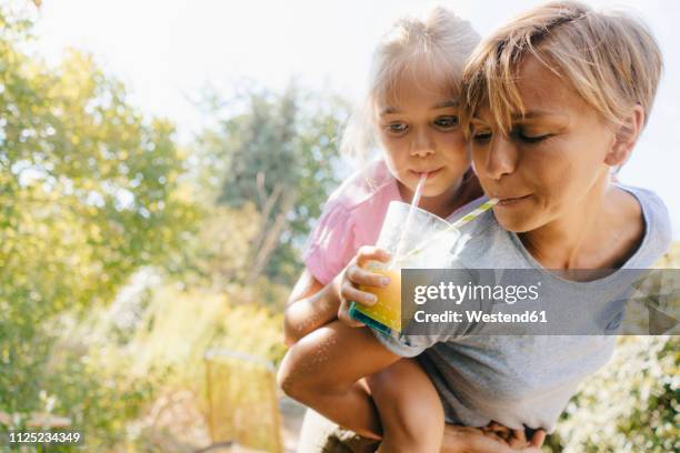 mother carrying daughter piggyback in garden drinking a smoothie - drinking smoothie stock pictures, royalty-free photos & images