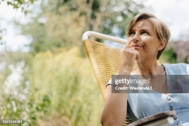 portrait of woman sitting in garden on chair - solo una donna di età media foto e immagini stock
