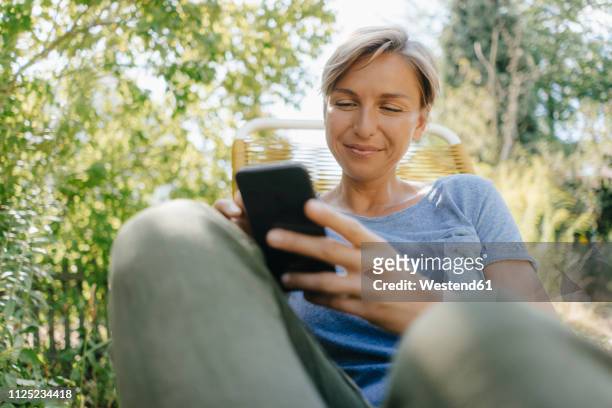 woman sitting in garden on chair using cell phone - mobile phone reading low angle stock-fotos und bilder