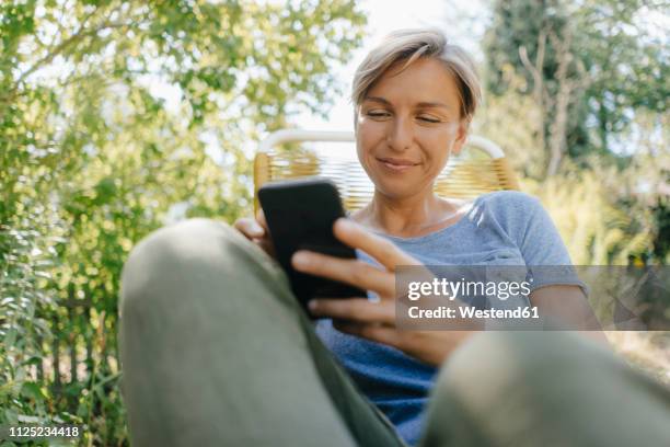 woman sitting in garden on chair using cell phone - women 35 foto e immagini stock