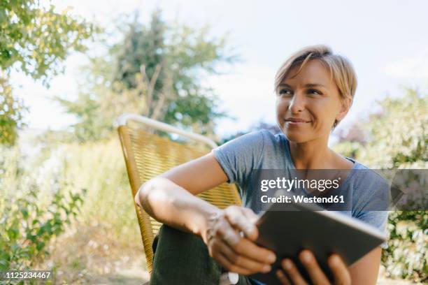 woman sitting in garden on chair holding tablet - 35 female outdoors stock pictures, royalty-free photos & images