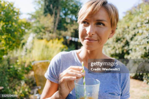 portrait of woman drinking a soft drink in garden - soft drink stock-fotos und bilder