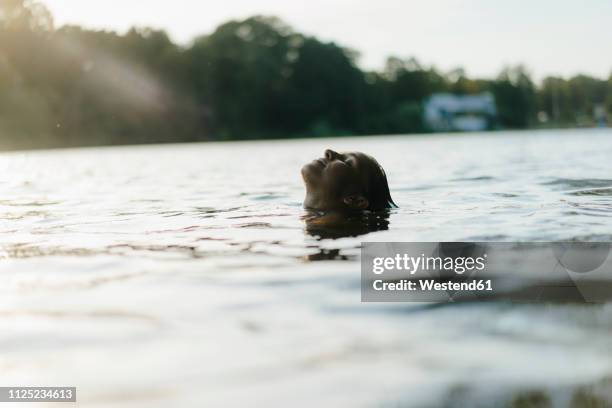 woman floating in a lake at sunset - bathing in sunset stockfoto's en -beelden