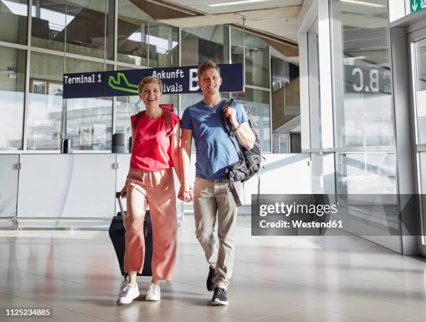 happy couple walking hand in hand at the airport - luggage trolley stock-fotos und bilder