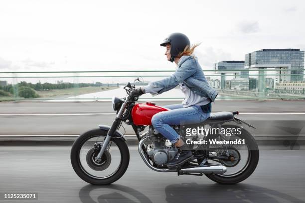 germany, cologne, young woman riding motorcycle on bridge - motorrad stock-fotos und bilder