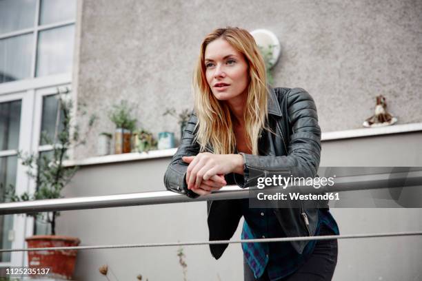 confident young woman wearing biker jacket leaning on balcony railing - garde corps photos et images de collection