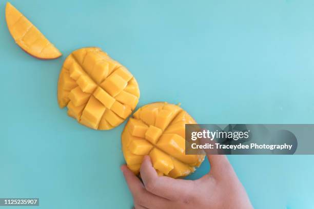 mango cut into three pieces with a hand taking a piece to eat. - mango tree stock pictures, royalty-free photos & images