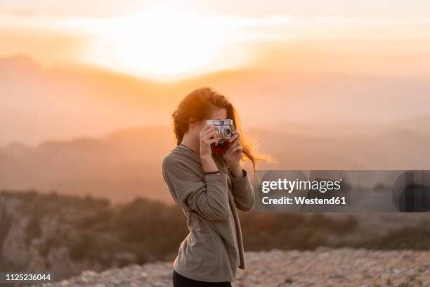 spain, barcelona, natural park of sant llorenc, woman taking a picture with vintage camera at sunset - frauen mit fotoapparat stock-fotos und bilder