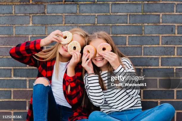 two girls having fun with doughnuts - brick wall hole stock pictures, royalty-free photos & images