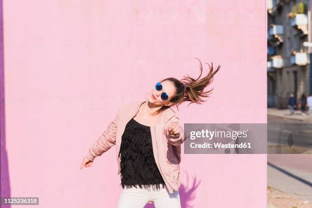 happy young woman moving in front of pink wall - workforce revolution stock-fotos und bilder