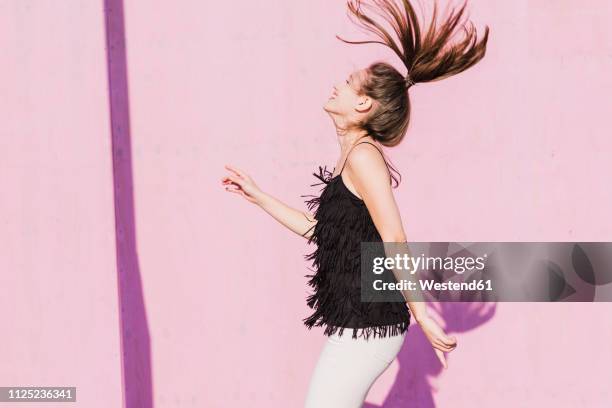 happy young woman moving in front of pink wall - quaste stock-fotos und bilder