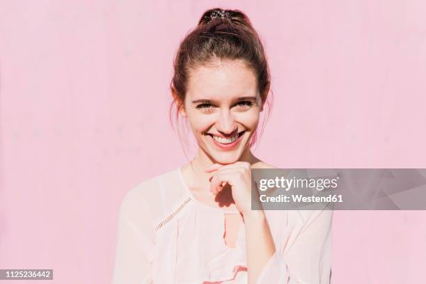 portrait of smiling young woman in front of pink wall - pink blouse stock-fotos und bilder