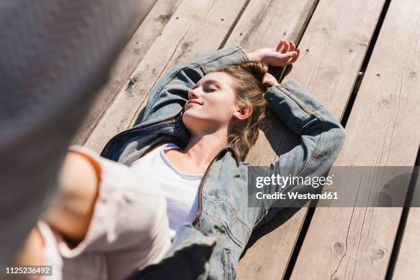 relaxed young woman lying on wooden boards in sunshine - sonnenbaden stock-fotos und bilder