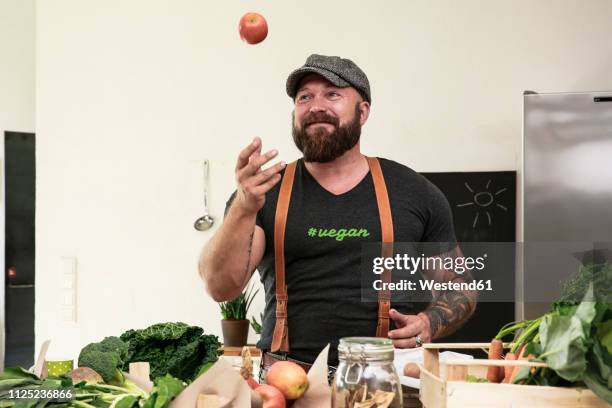 vegan man juggling with apples in his kitchen - vegan food fotografías e imágenes de stock