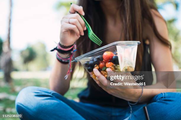 young woman sitting in a park, eating salad - recipiente de plástico fotografías e imágenes de stock