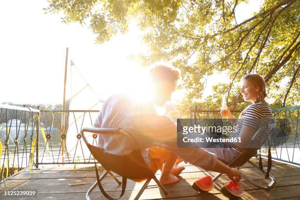 young couple sitting on a jetty at a lake eating watermelon - couple jetty stock pictures, royalty-free photos & images
