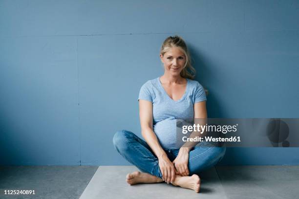 portrait of smiling pregnant woman sitting on the floor - donne bionde scalze foto e immagini stock