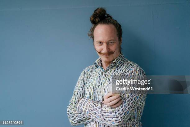 portrait of man with moustache standing at blue wall - eccentrico foto e immagini stock