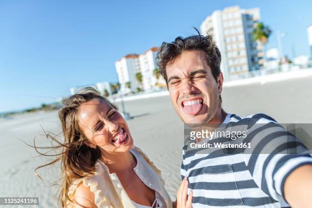 funny selfie of a happy young couple on the beach - sticking out tongue stock-fotos und bilder