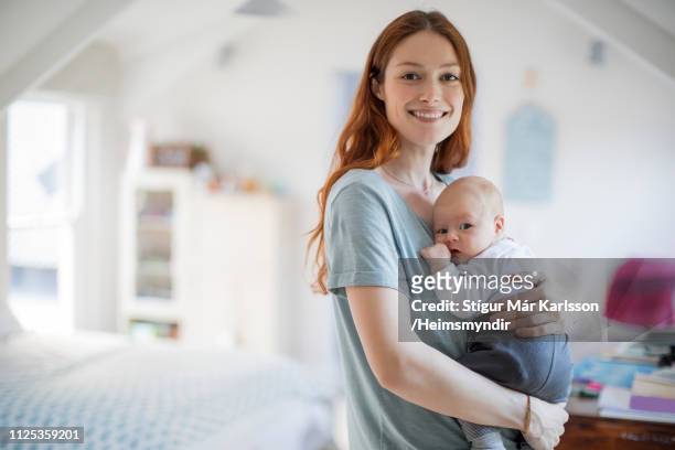 smiling redhead mother carrying son at home - baby mom stock pictures, royalty-free photos & images