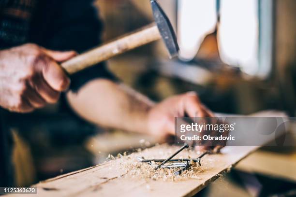 close up of man hammering a nail into wooden board - man builds his own plane imagens e fotografias de stock
