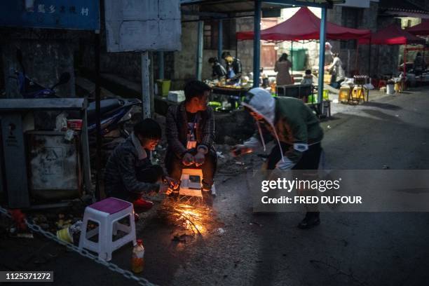 This photo taken on February 14, 2019 shows people getting warm around a small fire as they wait to sell food and goods prior to the annual flower...