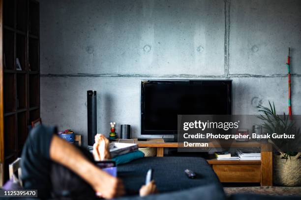 rear view of a man watching television in a living room - television stock-fotos und bilder