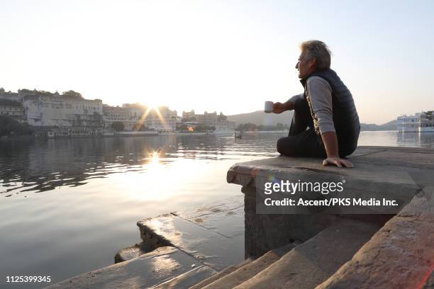 man relaxes on stone ghat above lake, sunrise - tee indien trinken stock-fotos und bilder