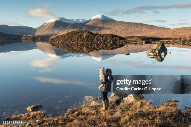 mother holding baby glancing at mountain range reflected on loch etive in glen etive, highlands of scotland, united kingdom - scotland winter stock pictures, royalty-free photos & images
