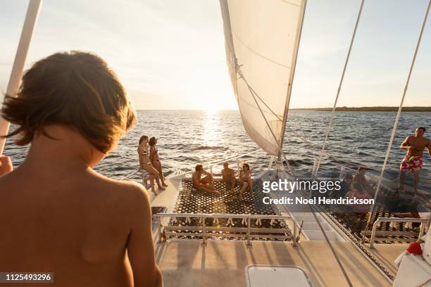 young boy on boat overlooking the sunset - catamaran sailing stock-fotos und bilder