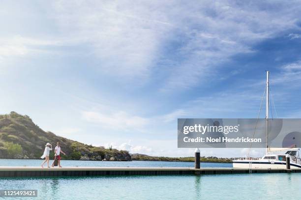 couple walking on pier in sunlight against bright blue sky - katamaran segeln stock-fotos und bilder
