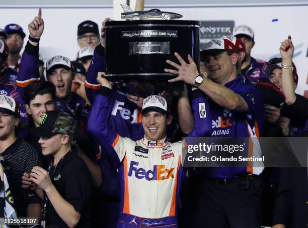 Denny Hamlin hoists the championship trophy as he celebrates in Victory Lane after winning the Daytona 500 NASCAR race at Daytona International...