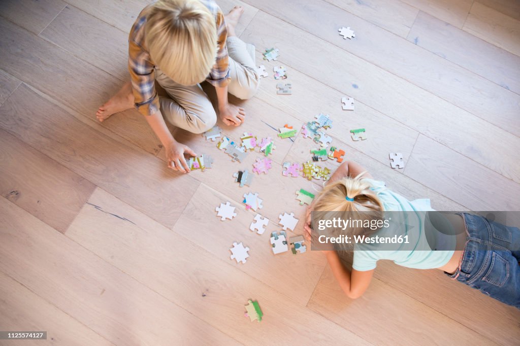 Brother and sister lying on the floor at home playing jigsaw puzzle