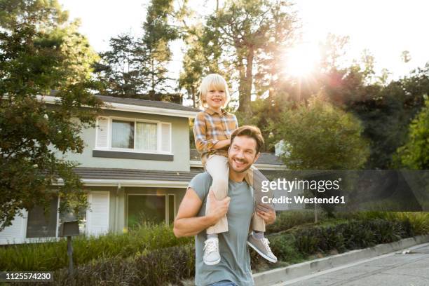 happy boy on father's shoulders in front of their home - family in front of house stock-fotos und bilder
