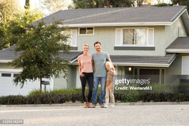 portrait of smiling parents with boy standing in front of their home - dreiviertel vorderansicht stock-fotos und bilder