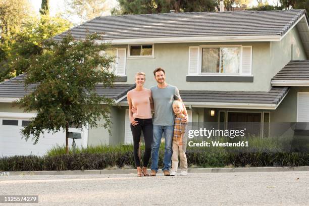 portrait of smiling parents with boy standing in front of their home - stéréotype de la classe moyenne photos et images de collection