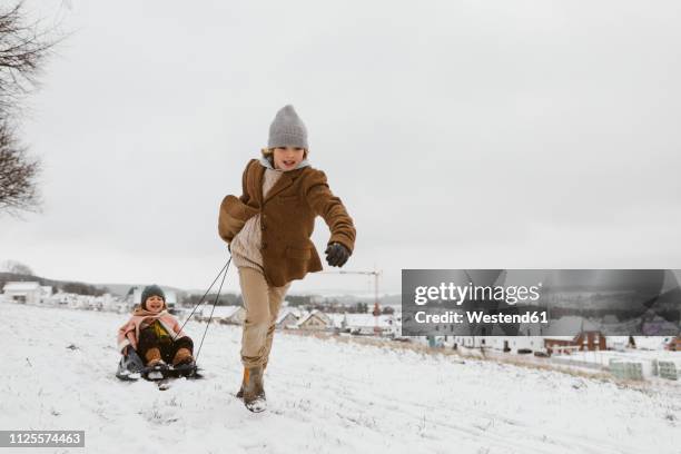 boy pulling sledge with little sister in snow - sledge fotografías e imágenes de stock