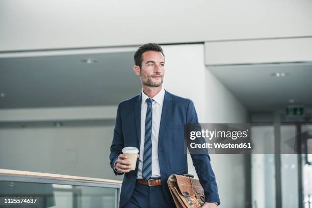 businessman with briefcase walking in office building, holding cup of coffee - a buisness man with a brifecase stock-fotos und bilder