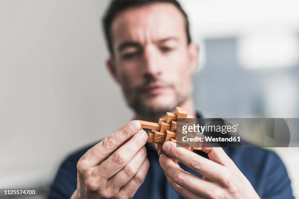 mature man sitting in office assembling wooden cube puzzle - herausforderung stock-fotos und bilder