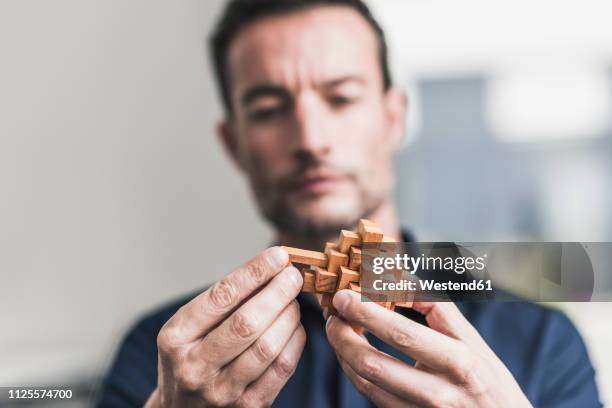 mature man sitting in office assembling wooden cube puzzle - complessità foto e immagini stock