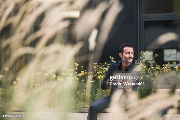 businessman sitting outside, taking a break, drinking coffee, using digital tablet - business outdoor stockfoto's en -beelden